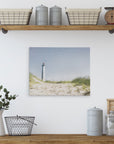 Nestled in a minimalist kitchen shelf setup adorned with rustic decor and coastal prints from Offley Green, the top shelf features two baskets, two metal jars, and a vintage scale. Below hangs an 11x14 Coastal Canvas Print of a lighthouse from Offley Green's collection. On the countertop, you'll find a metal basket, a ceramic pitcher with plants, and additional metal jars.