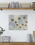 A minimalist kitchen shelf setup with various items including wicker baskets, metal canisters, a small vintage scale, a white pitcher holding green foliage, and a wire basket. Above the shelf, an Offley Green 11x14 California Canvas Print (Choose from 10+ Designs) depicts tall palm trees against a blue sky, reminiscent of California prints.