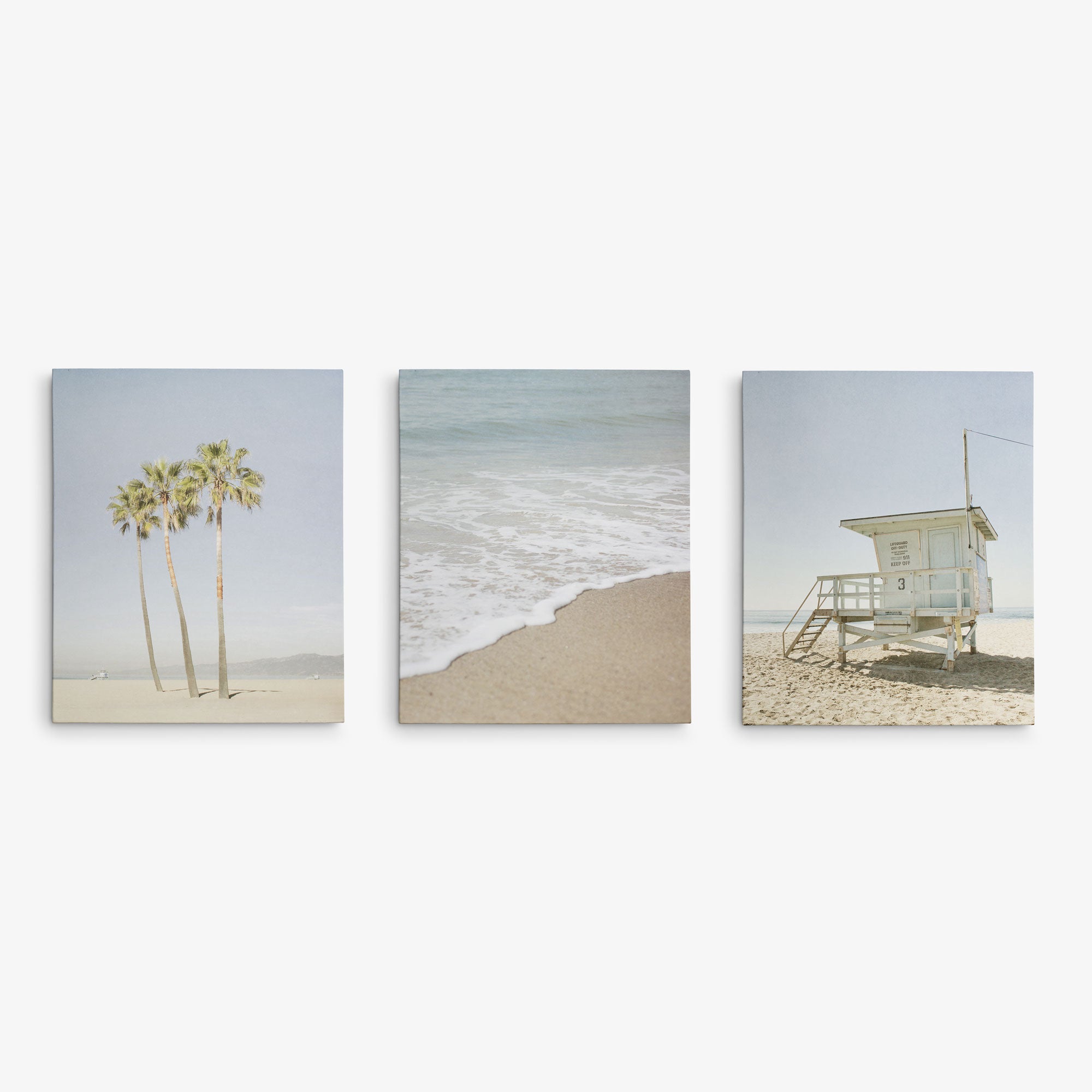 The Offley Green Set of 3 Canvas includes a left image of palm trees on sand, a center photo of ocean waves hitting the shore, and a right scene featuring a lifeguard tower. Each artist-grade canvas captures the tranquil coastal vibe perfectly.