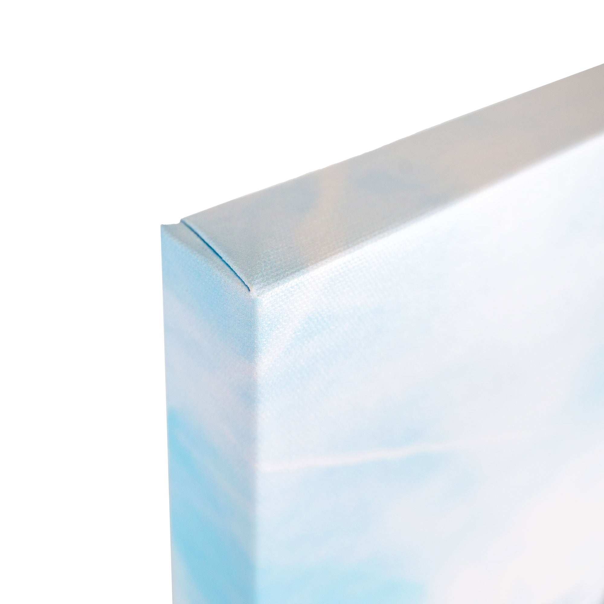 A close-up image of the corner of an 8x10 California Canvas Print from Offley Green reveals its white and light blue sky-themed artwork. The canvas is tightly wrapped around the wooden frame, showcasing a pristine gallery wrap with the corner neatly folded and secured. This high-quality print is one of over 10 designs available from Offley Green.