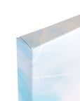 A close-up image of the corner of an 8x10 California Canvas Print from Offley Green reveals its white and light blue sky-themed artwork. The canvas is tightly wrapped around the wooden frame, showcasing a pristine gallery wrap with the corner neatly folded and secured. This high-quality print is one of over 10 designs available from Offley Green.