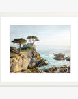 The California Coastal Print, 'Lone Cypress' by Offley Green features a framed photograph of a coastal cliff at Pebble Beach. It depicts two windswept cypress trees perched at the edge, overlooking the ocean. The water appears vibrant blue with white waves crashing against the rocky shore under a clear, light blue sky. This setting evokes serene natural beauty.