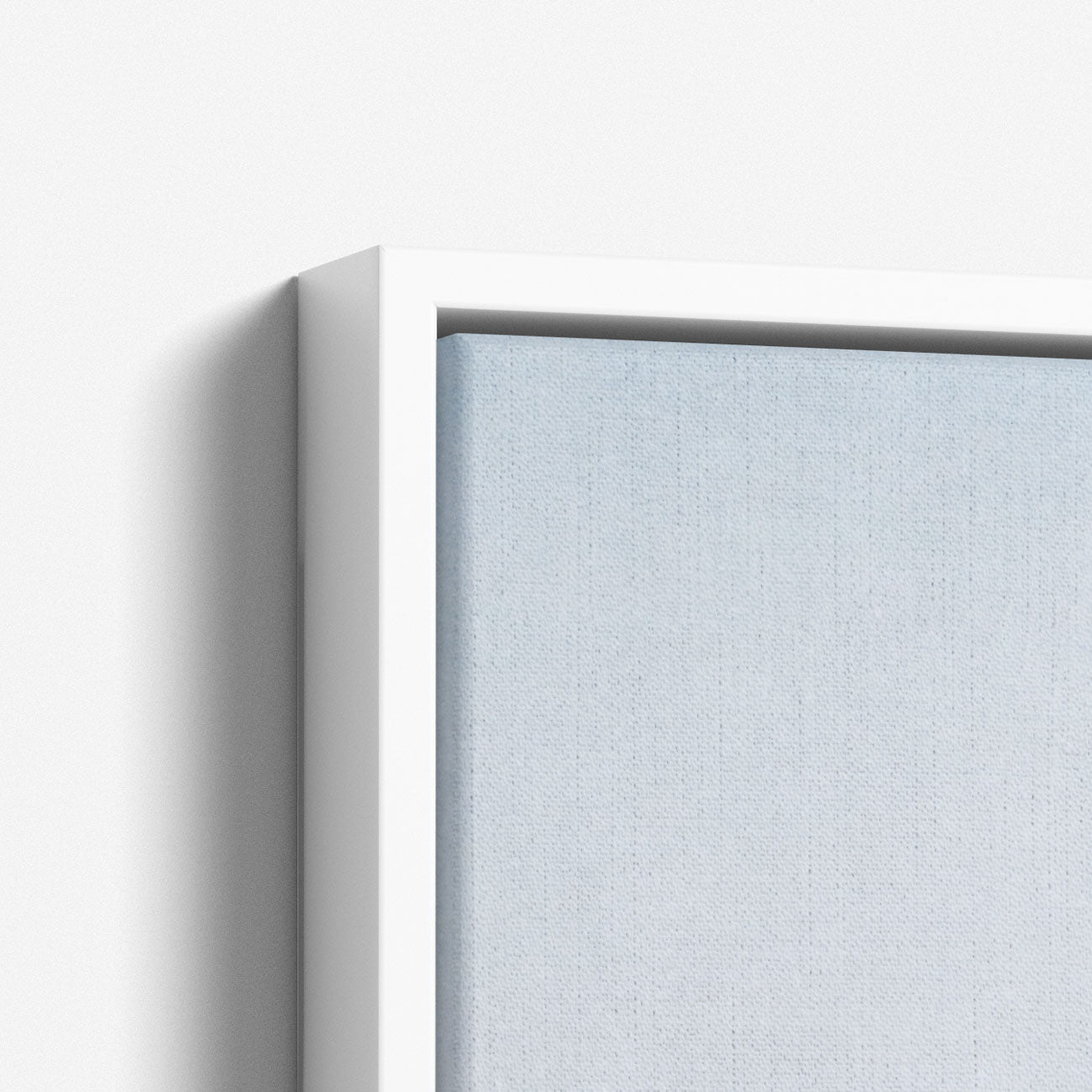 Close-up view of the corner of a white-framed canvas print hanging on a wall. This framed piece from Offley Green&#39;s Set of 4 Framed Canvas collection features artwork with a delicate gradient transitioning from light blue to light grey, evoking coastal styles and creating a minimalist, serene impression. The background wall is white.