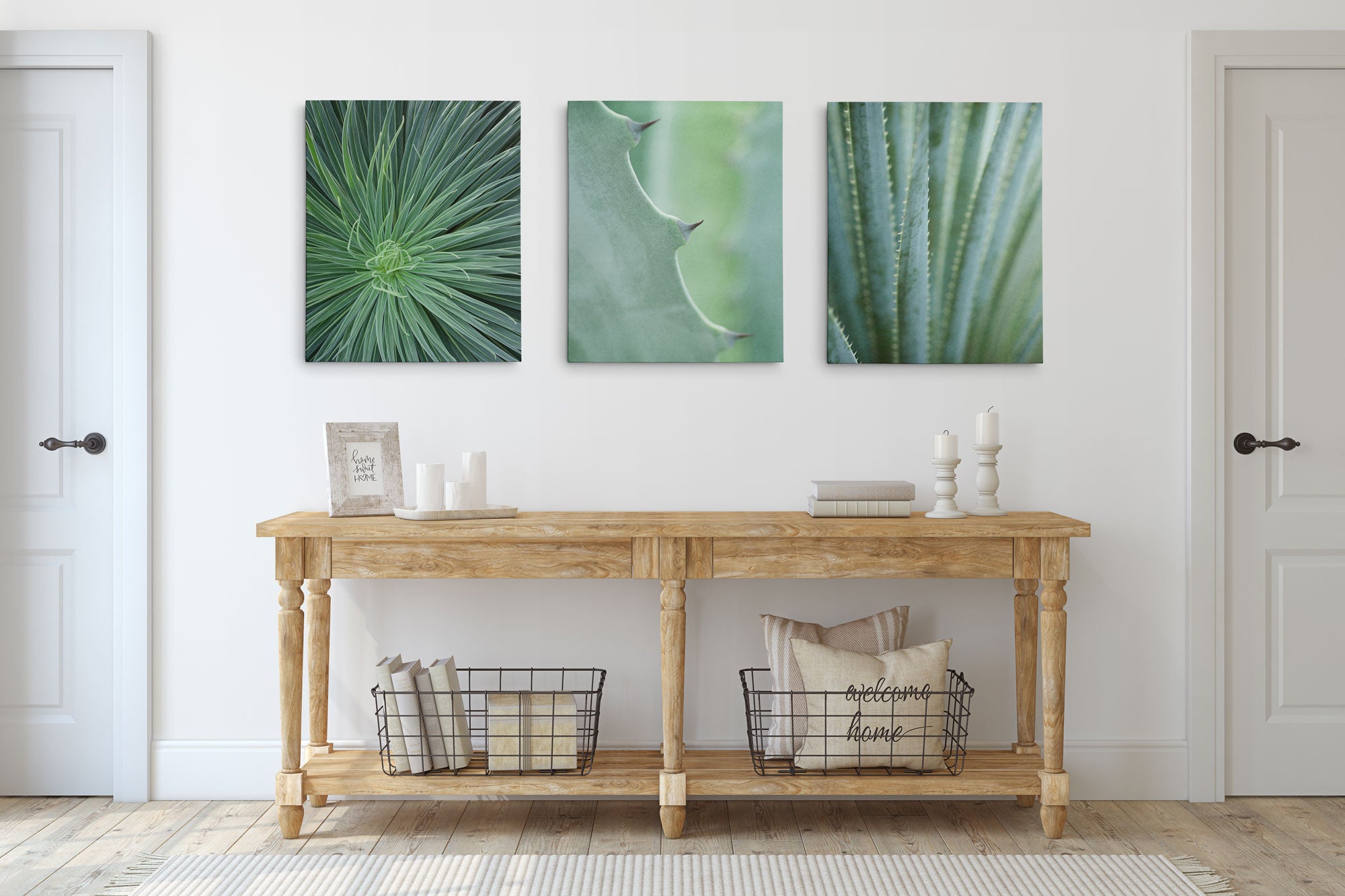 A minimalist room includes a wooden console table with wire baskets and pillows. Above it, Offley Green&#39;s Set of 3 Canvas prints feature botanical close-ups of green plant textures. The white wood walls and doors, made from FSC certified forests, enhance the calm atmosphere.