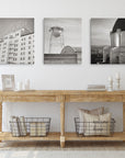 The room features a wooden console table with candles, books, and baskets holding pillows. Above it, the Offley Green Set of 3 Canvas displays black and white photos of a hotel, water tower, and observatory. White walls and doors elegantly frame the space.