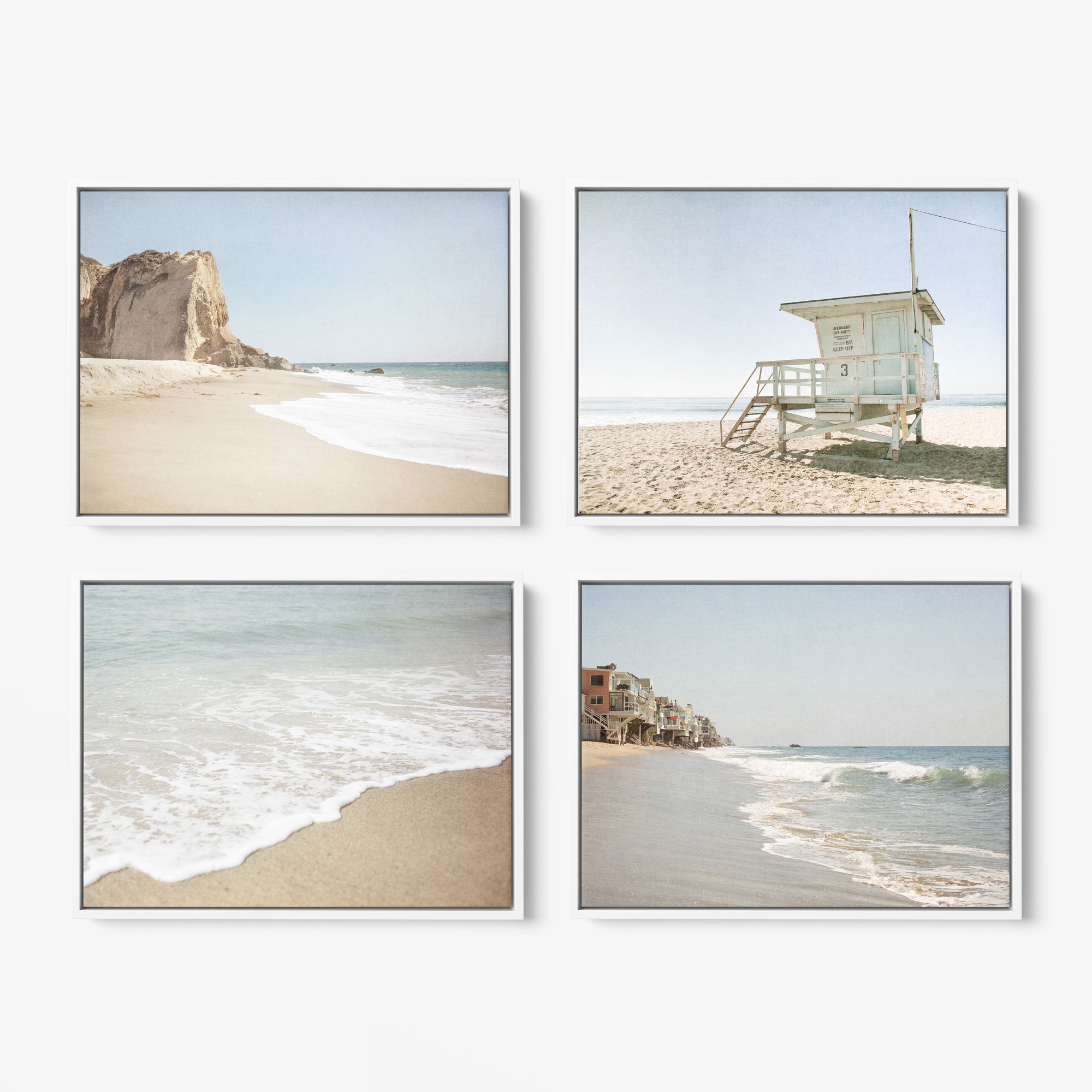 The Set of 4 Framed Canvas by Offley Green is arranged in a grid, showcasing beach scenes. The top left canvas depicts a rocky cliff by the ocean, while the top right features a lifeguard tower. The bottom left canvas captures gentle waves on the shore, and the bottom right exhibits a beachfront with houses that evoke relaxing coastal styles.