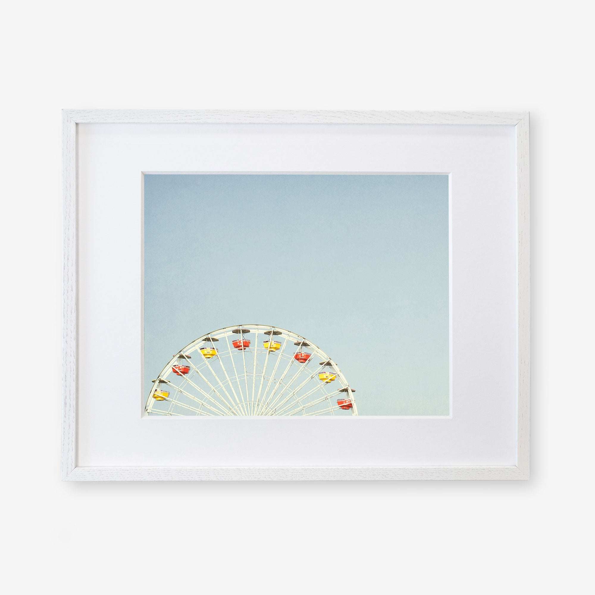 A partially visible &#39;Ferris Blue&#39; wall decor at Santa Monica Pier with white spokes and yellow and red gondolas against a clear blue sky by Offley Green.