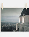 Photo of a cityscape at dusk pinned to a line, with Offley Green's Griffith Observatory Print, 'The Sky At Night' in the foreground and twinkling city lights below a starry sky.