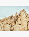 Rugged and textured rock formations in Joshua Tree rise steeply under a clear sky, with sharp peaks and large, rounded boulders covering the landscape. This scene is captured beautifully in the Offley Green 'Joshua Rocks' print.