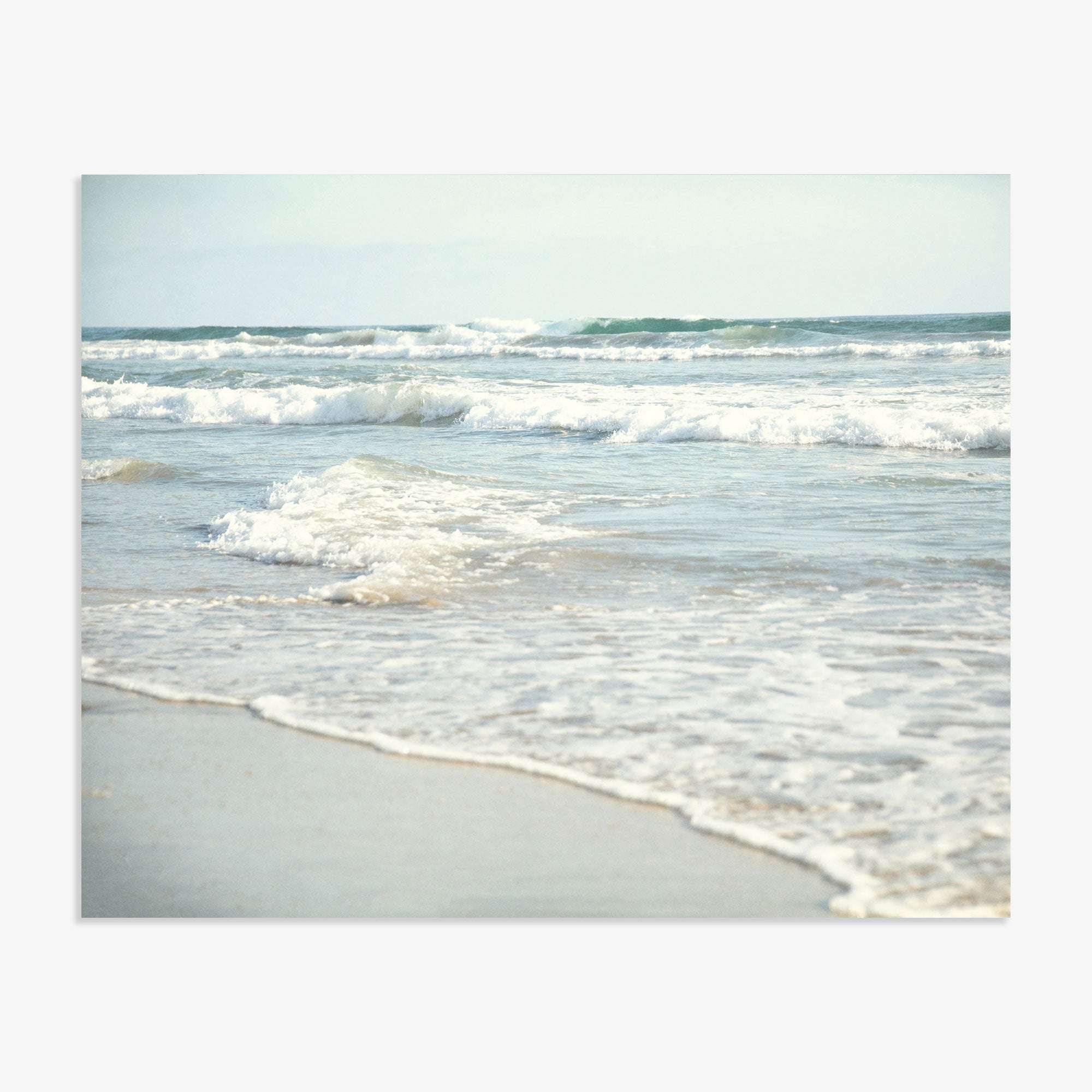 Ocean waves roll onto Carlsbad State Beach, capturing the dynamic movement of water with a backdrop of a hazy, overcast sky featuring the Coastal Beach Print in California &#39;Surf and Sun&#39; by Offley Green.