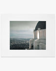 A nighttime photograph framed in white, showcasing the Los Angeles city view from Offley Green's Griffith Observatory Print, 'The Sky At Night', with twinkling lights under a starry sky.