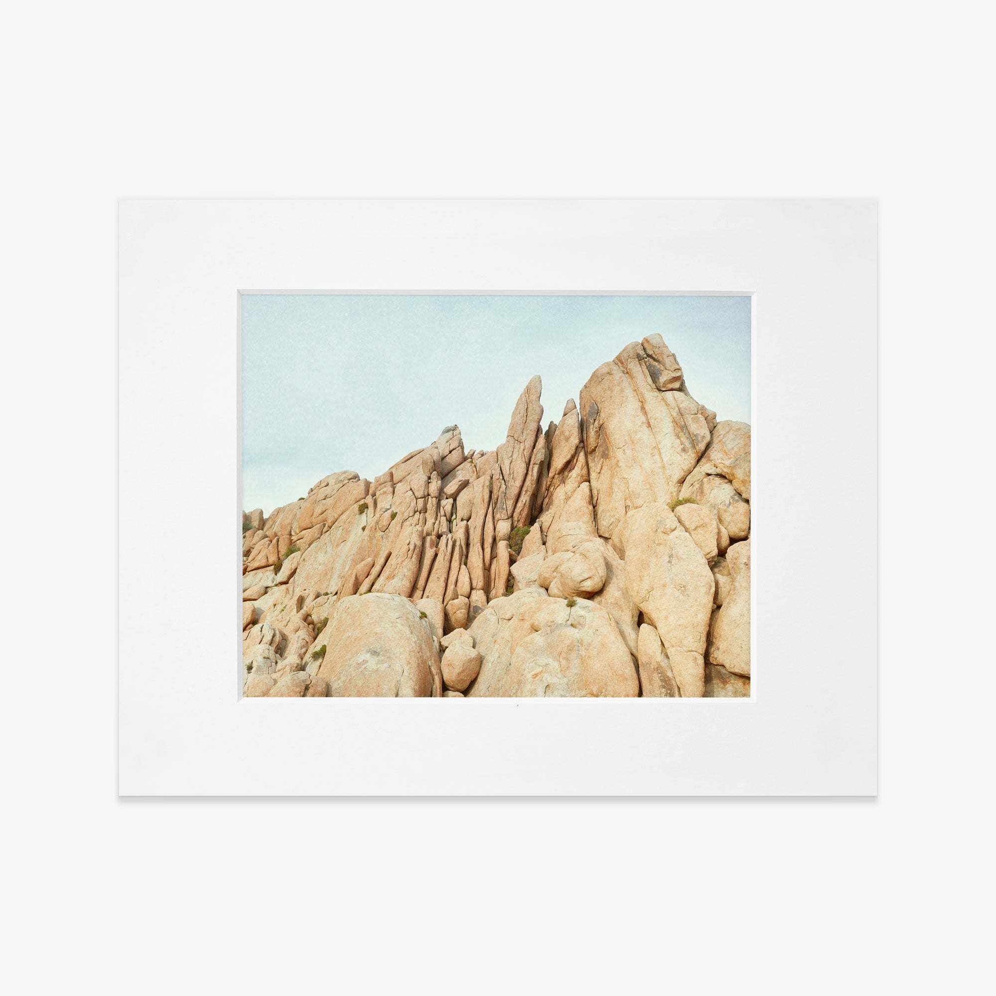 A framed photograph of a rugged desert landscape featuring large, weathered rock formations under a clear sky. The image is centered within a white matting inside an Offley Green frame and printed on archival photographic paper.