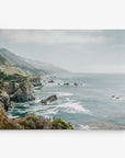 Experience the serene beauty of a rugged shoreline with cliffs and rocky outcrops extending into the ocean captured on the 11x14 Coastal Canvas Print from Offley Green. The calm water with gentle waves and a hint of mist over distant mountains and hills provides a picturesque scene, while lush vegetation adds greenery to the landscape. Choose from 10+ designs for the perfect coastal print to enhance your space.