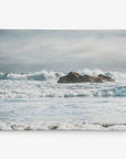 A rocky outcrop is surrounded by ocean waves, which appear rough and choppy. The horizon is somewhat obscured by a mist or haze, giving the scene a serene yet powerful ambiance. The sky above is mostly cloudy, adding to the dramatic mood of this seascape—a perfect subject for Offley Green's 8x10 Coastal Canvas Print (Choose from 10+ Designs) as wall art.