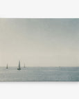 A serene seascape featuring several sailboats scattered across calm, open waters. The horizon blends softly with the sky, which is lightly overcast, casting a peaceful, muted light over the scene. This Offley Green "11x14 Coastal Canvas Print" (Choose from 10+ Designs) comes as a ready-to-hang canvas gallery wrap.