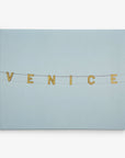 A clear sky with string lights spelling out "VENICE" hanging on black wires. The background is a gradient of light blue, creating a calm and serene atmosphere, reminiscent of Offley Green's 11x14 California Canvas Print (Choose from 10+ Designs) wall art or even a canvas gallery wrap.