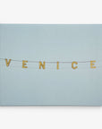 A photograph from Offley Green's 8x10 California Canvas Print collection (Choose from 10+ Designs), displaying the word "VENICE" in illuminated letters strung on wires against a serene pale blue sky background, making it an ideal wall art piece to bring a touch of the Californian coast into your home.