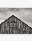 A monochrome photo depicts the upper portion of a weathered wooden barn with a small window in the center. The sky above is overcast with clouds, creating a somber and rustic atmosphere perfect for an 11x14 Rustic Canvas Print (Choose from 10+ Designs) by Offley Green.