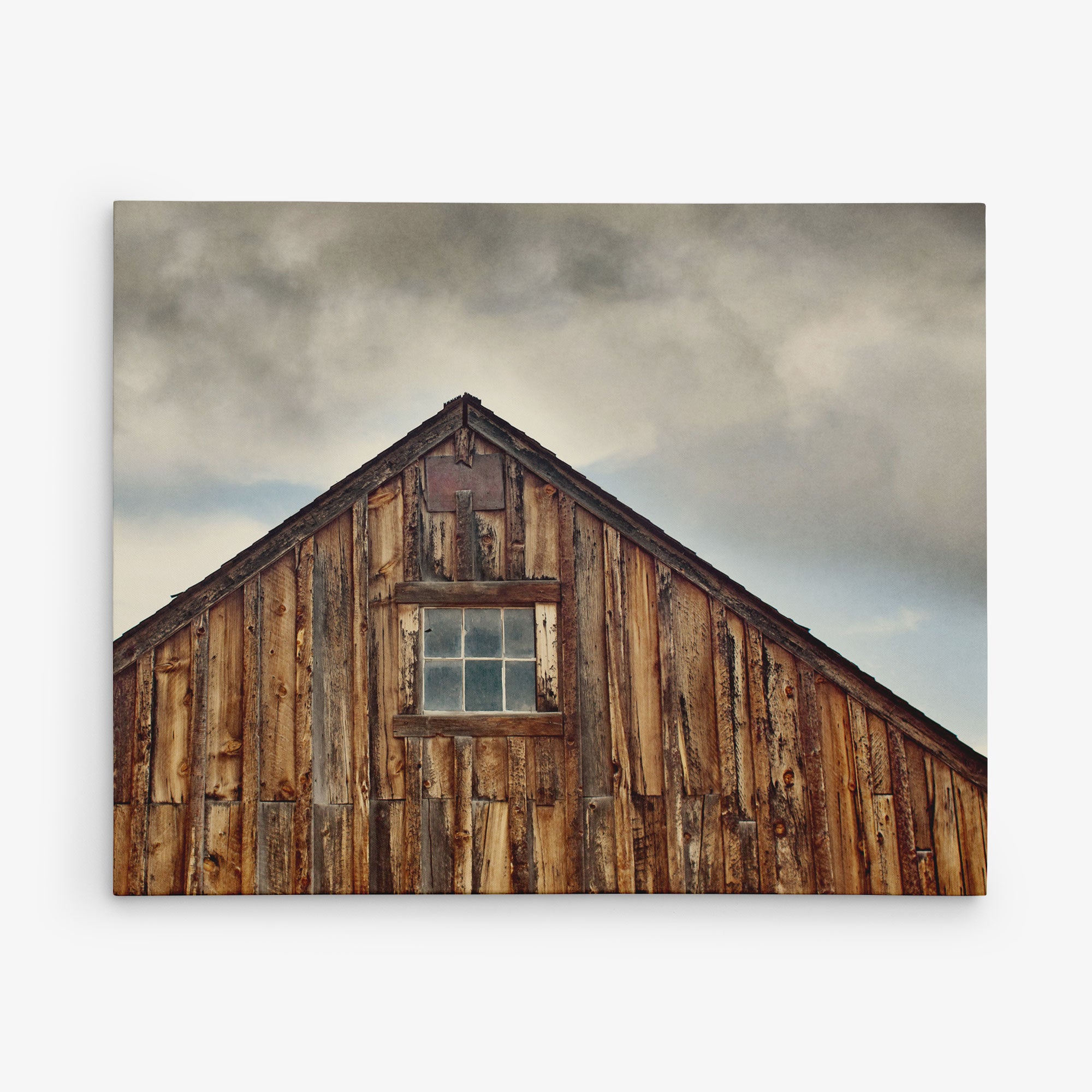 The image shows the weathered wooden roof of a rustic barn against a cloudy sky. The peak of the roof features a small, rectangular window with divided panes, highlighting the texture and aged appearance of the barn&#39;s wood—perfect for creating stunning Offley Green 11x14 Rustic Canvas Print (Choose from 10+ Designs).