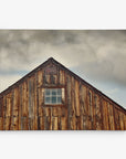 The image shows the weathered wooden roof of a rustic barn against a cloudy sky. The peak of the roof features a small, rectangular window with divided panes, highlighting the texture and aged appearance of the barn's wood—perfect for creating stunning Offley Green 11x14 Rustic Canvas Print (Choose from 10+ Designs).