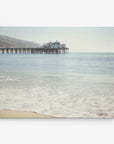 A tranquil beach scene featuring a long wooden pier extending into calm ocean waters graces this 8x10 California Canvas Print from Offley Green. The clear sky and faintly visible distant hills add to the serenity, as gentle waves wash onto the sandy shore. This stunning image, perfect for any of the 10+ designs available, would make beautiful wall art in any space.