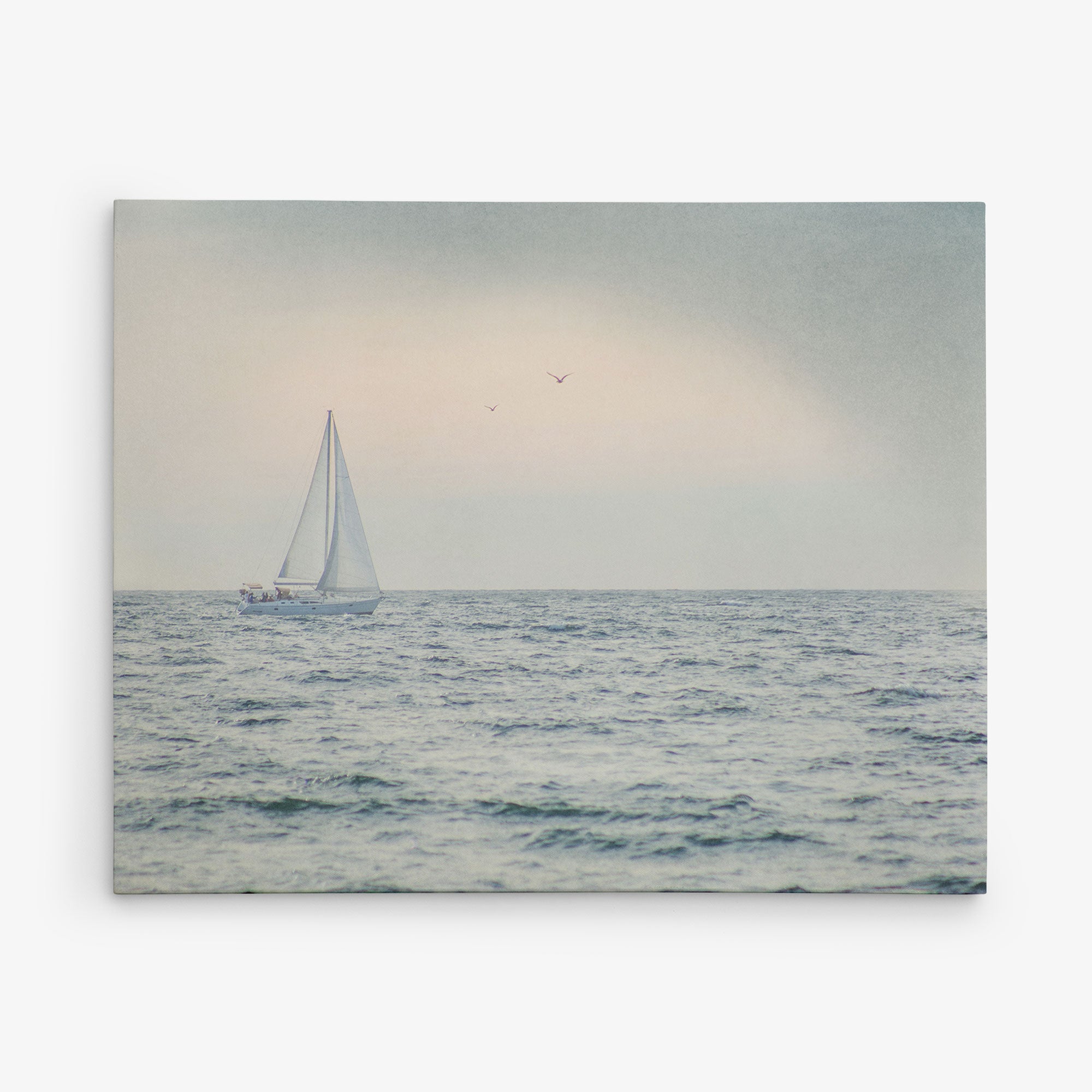 A serene seascape featuring a solitary sailboat with white sails gliding on calm waters under a hazy sky. Three birds are flying in the distance, enhancing the peaceful and tranquil atmosphere. This beautiful scene is captured on Offley Green&#39;s 11x14 Coastal Canvas Print (Choose from 10+ Designs) and comes ready to hang, making it perfect for any space.