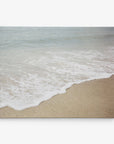 A tranquil beach scene showcasing gentle ocean waves softly rolling onto a sandy shore. The pale blue water seamlessly merges with the beige sand, fostering a serene and peaceful ambiance. Ideal as coastal prints or on an Offley Green 24x30 Coastal Canvas Print (Choose from 10+ Designs) to bring tranquility to any space.