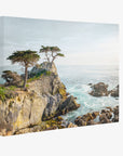 The Offley Green 11x14 Coastal Canvas Print, available in over ten designs, showcases a scenic coastal landscape with rocky cliffs and turquoise waves crashing below. Three resilient trees stand atop the cliff, reaching toward a partly cloudy sky. The sunlight highlights the natural beauty of the ocean and rocky shoreline, making it ready to hang.