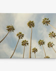 The Offley Green 8x10 California Canvas Print, featuring a view of tall palm trees with lush green fronds set against a pale blue sky with wispy clouds, captures the warm, slightly faded vintage essence of classic California prints. This gallery wrap wall art is available in over 10 designs to perfectly complement any space.