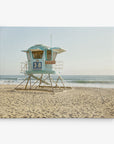 A serene 30x40 California Canvas Print by Offley Green features a light blue lifeguard tower numbered "38" on a sandy beach, with the ocean and gentle waves in the background. The clear sky hints at a calm, sunny day, making it an ideal piece of wall art reminiscent of classic California prints. Choose from over 10 stunning designs to capture this perfect beach scene in your home.