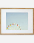 A framed photograph of Ferris Blue, the Santa Monica Pier ferris wheel, partially visible at the bottom, against a light blue sky, displayed in a simple wooden frame with a white mat by Offley Green.