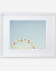 A framed image showcasing the top half of a ferris wheel with colorful gondolas against a pale blue sky, captured on archival photographic paper, centered within a white mat and a simple white frame of Offley Green's Blue Minimalist Wall Decor, 'Ferris Blue'.