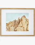 Framed photograph of a Offley Green Joshua Tree Print, 'Joshua Rocks' desert landscape, featuring tall, jagged rock formations under a clear blue sky, displayed in a natural wood frame with a white mat border.
