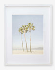 A framed photograph of three tall palm trees under a clear sky, taken at Venice Beach, with a sandy beach and distant hills visible at the base of the palms - Offley Green California Venice Beach Print, 'Three Palms'.