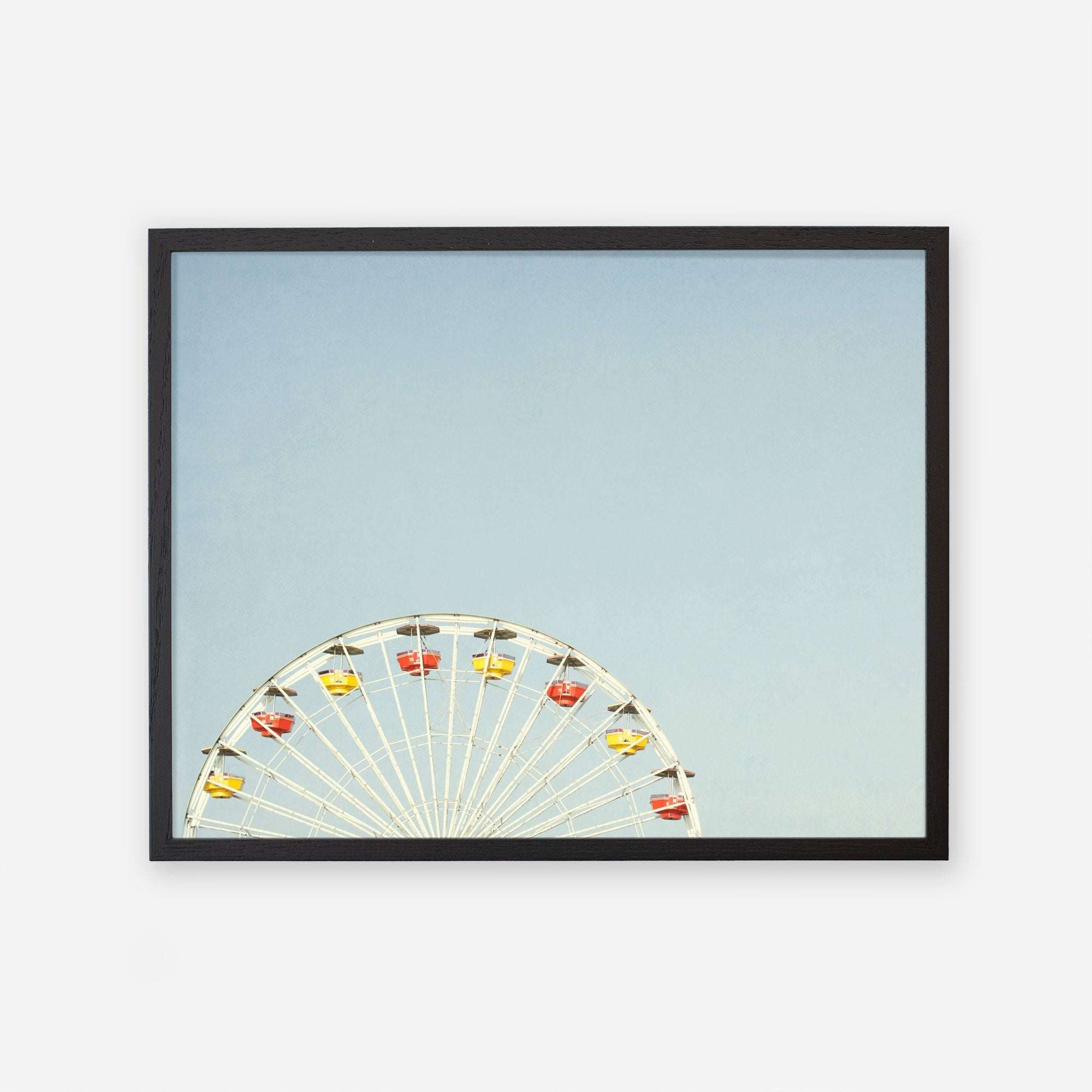 A Blue Minimalist Wall Decor print on archival photographic paper, depicting the top half of a colorful ferris wheel against a clear blue sky, giving a sense of a calm and cheerful day at a fair. Introducing &#39;Ferris Blue&#39; from Offley Green.