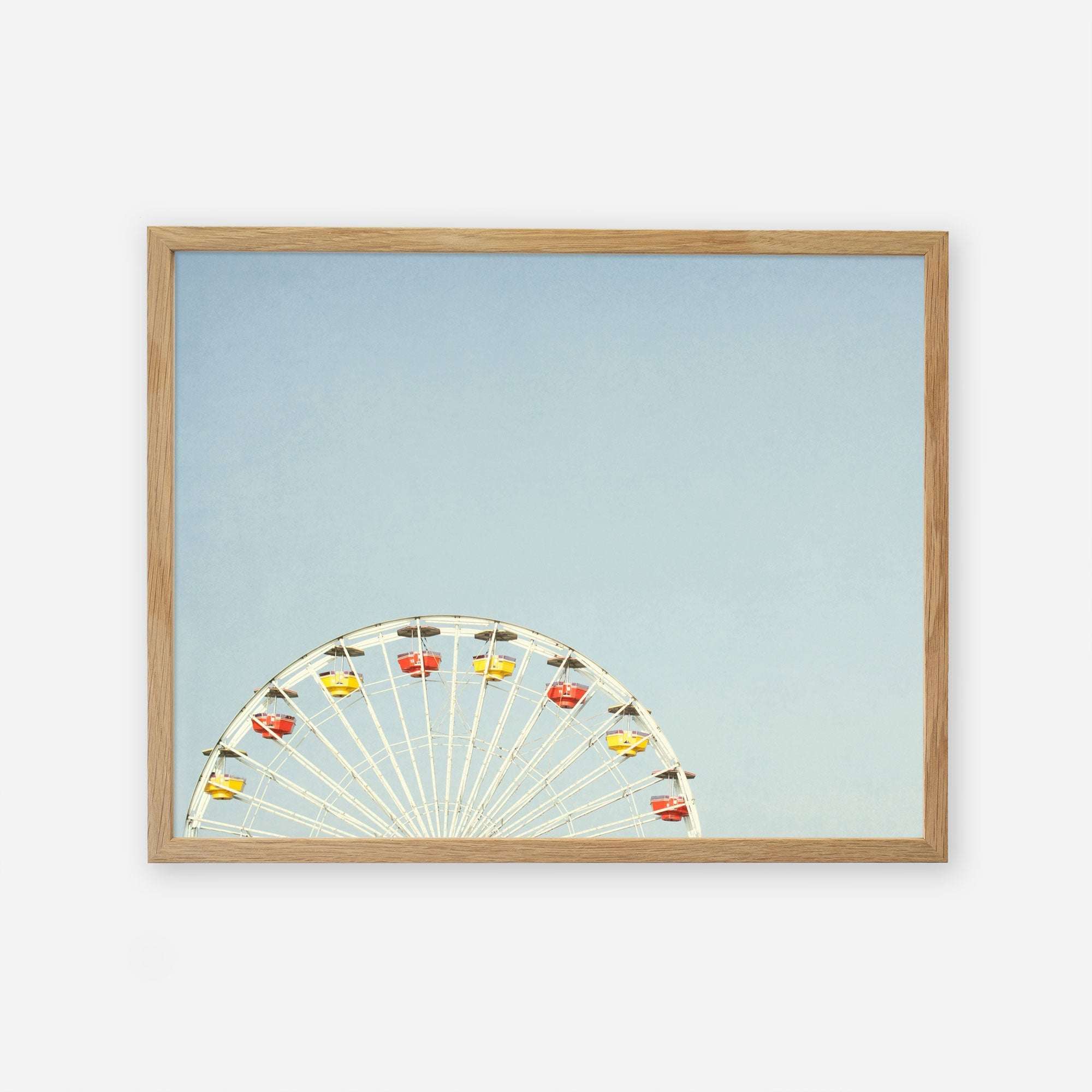 A framed picture showing the top half of a Ferris wheel with colorful cabins against a clear blue sky background, captured on archival photographic paper. This is the Blue Minimalist Wall Decor, &#39;Ferris Blue&#39; by Offley Green.