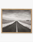 A framed Offley Green black and white photograph on archival photographic paper of a straight road leading through a rural landscape with fenced fields and sparse trees under a cloudy sky, titled 'American Road Trip'.