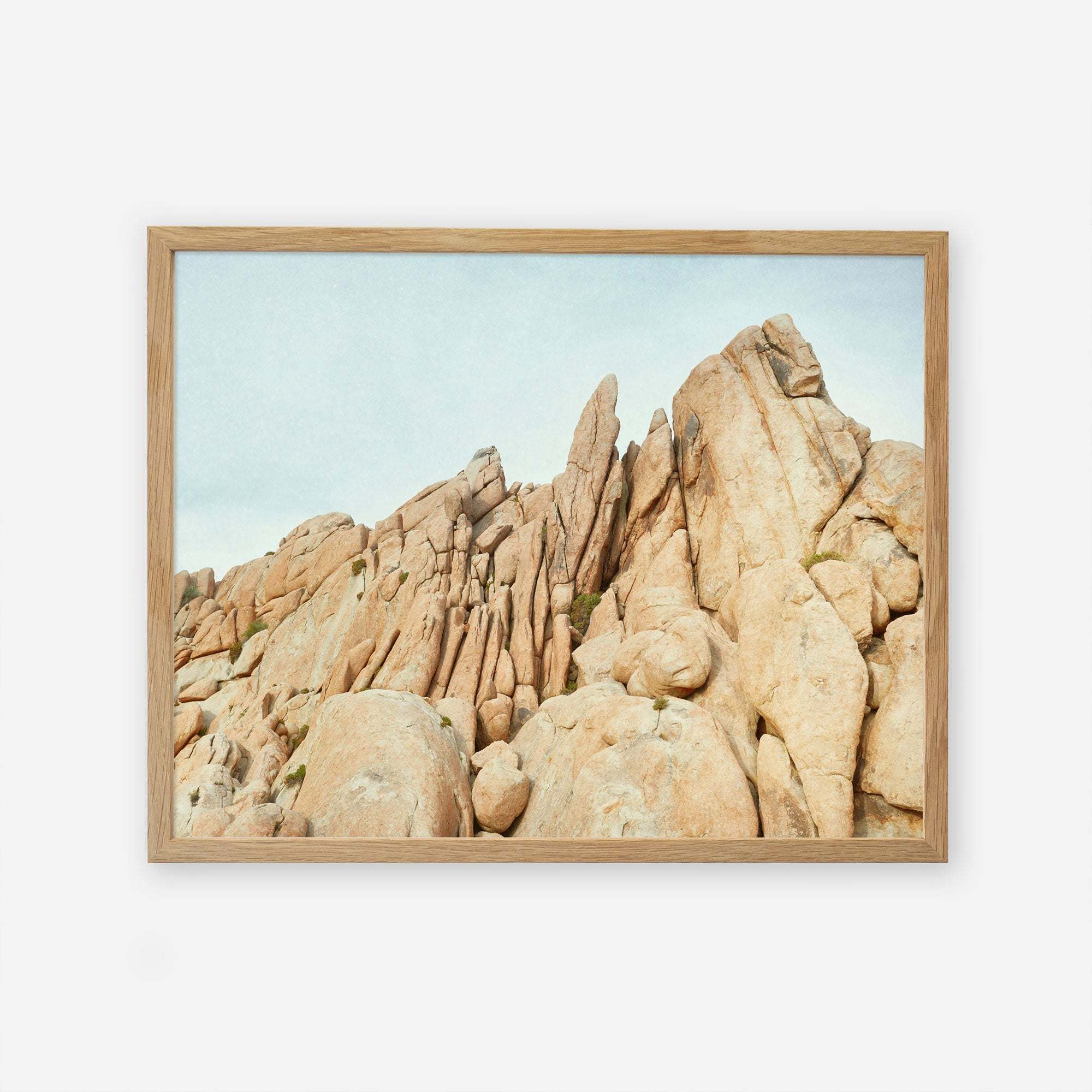 A framed photograph of a rugged rocky landscape featuring tall, narrow rock formations and boulders under a clear sky, printed on archival photographic paper. The frame is simple and made of light wood. This is the Offley Green &#39;Joshua Rocks&#39; Joshua Tree Print.
