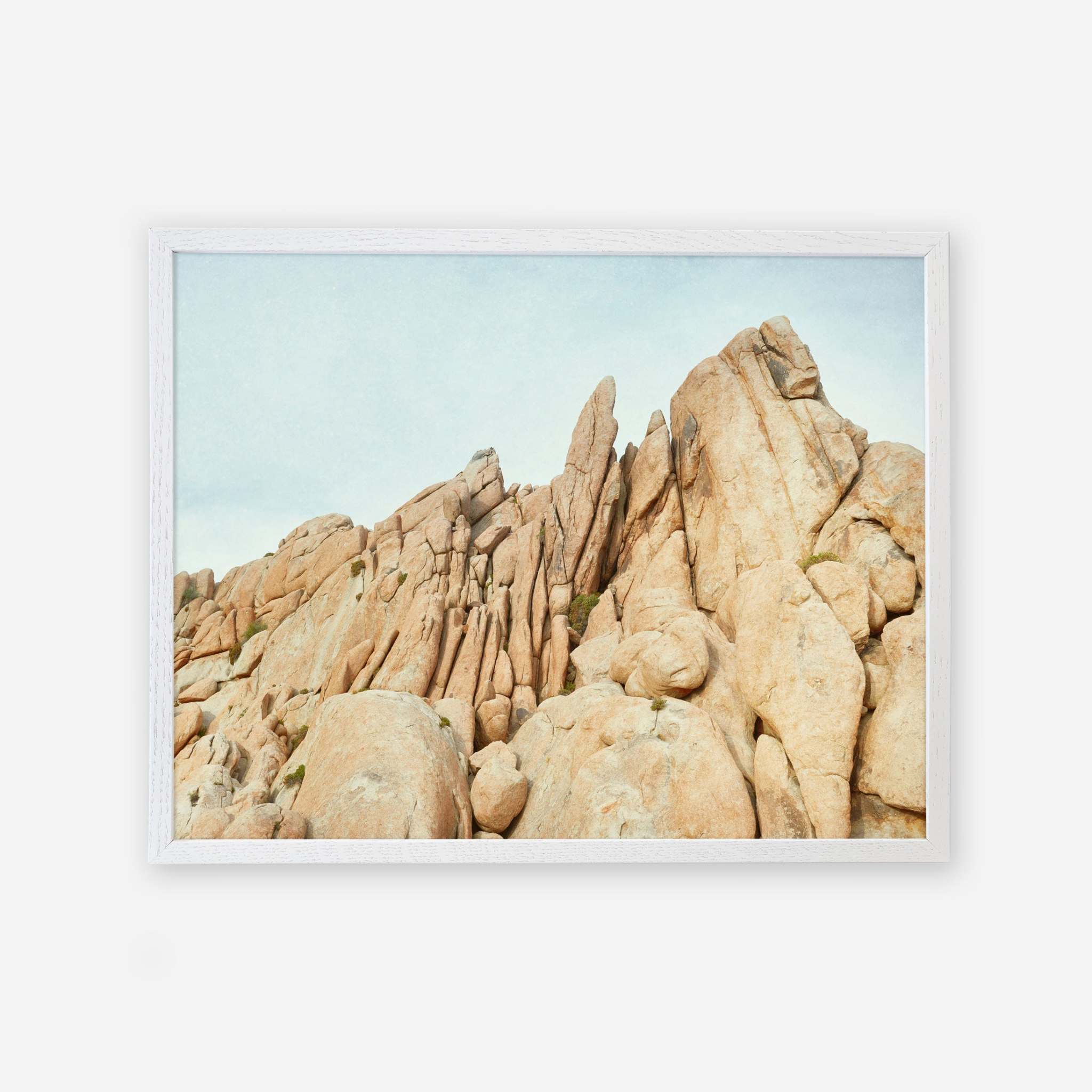 An unframed image of a rugged rock formation with sharp and rounded boulders extending towards a clear sky, depicted in a natural, earthy palette by Offley Green&#39;s Joshua Tree Print, &#39;Joshua Rocks.&#39;