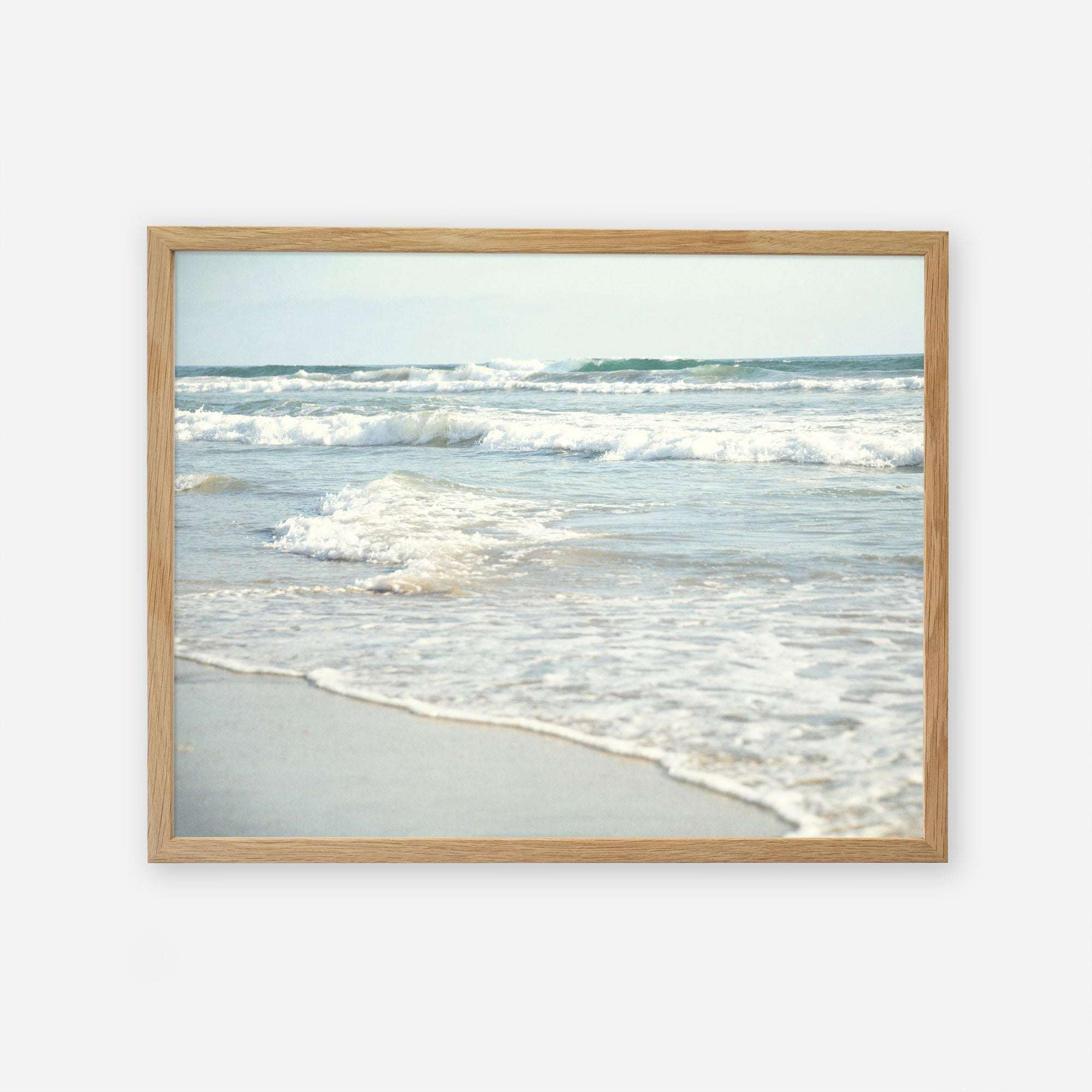 A framed photograph of Carlsbad State Beach displaying gentle waves breaking along the shoreline, with a blurred view of the ocean&#39;s horizon in the background, featuring the Coastal Beach Print in California &#39;Surf and Sun&#39; by Offley Green.