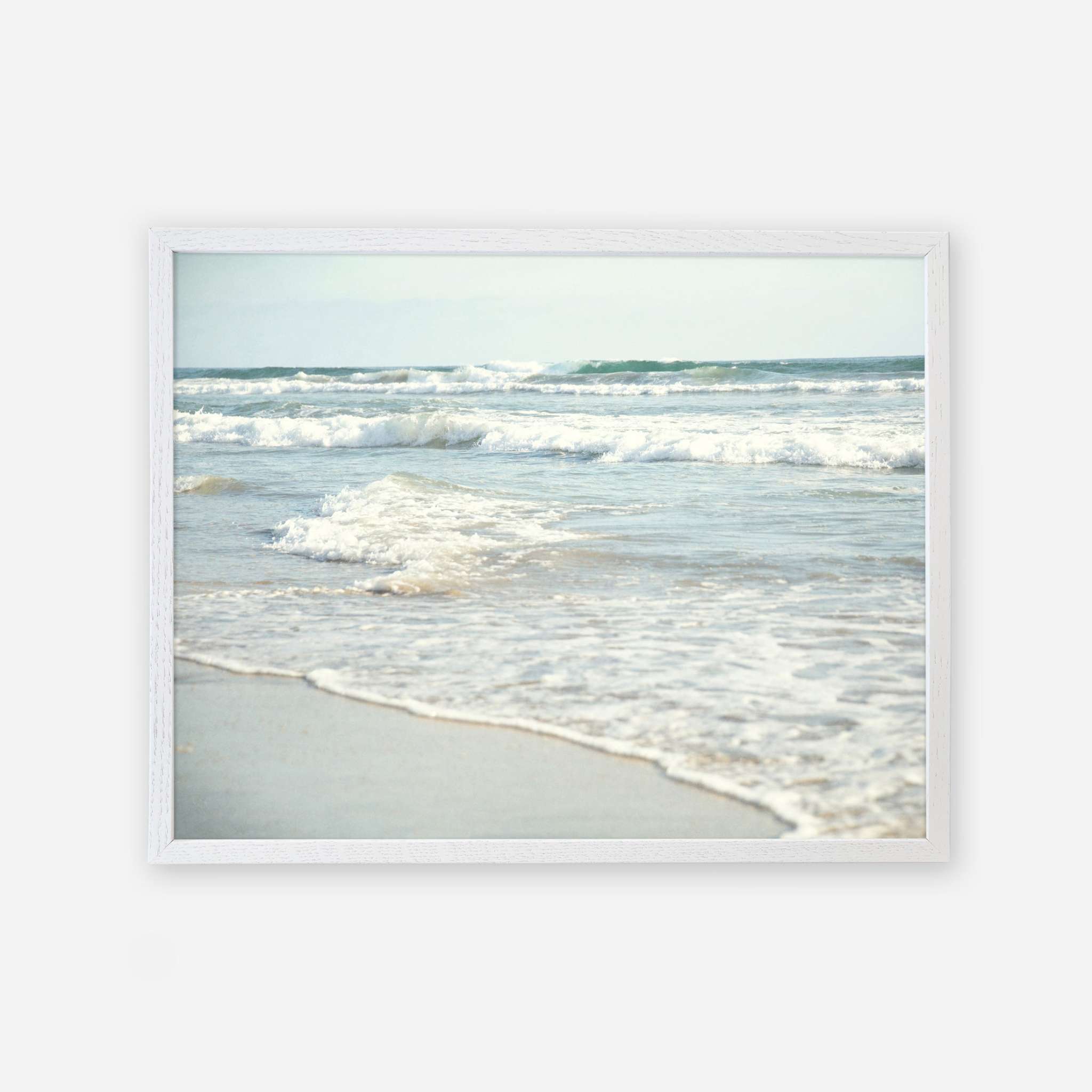 A framed photograph of a tranquil beach scene at Carlsbad State Beach, depicting gentle waves rolling onto the sandy shore under a clear sky, from Offley Green&#39;s Coastal Beach Print in California &#39;Surf and Sun&#39;.