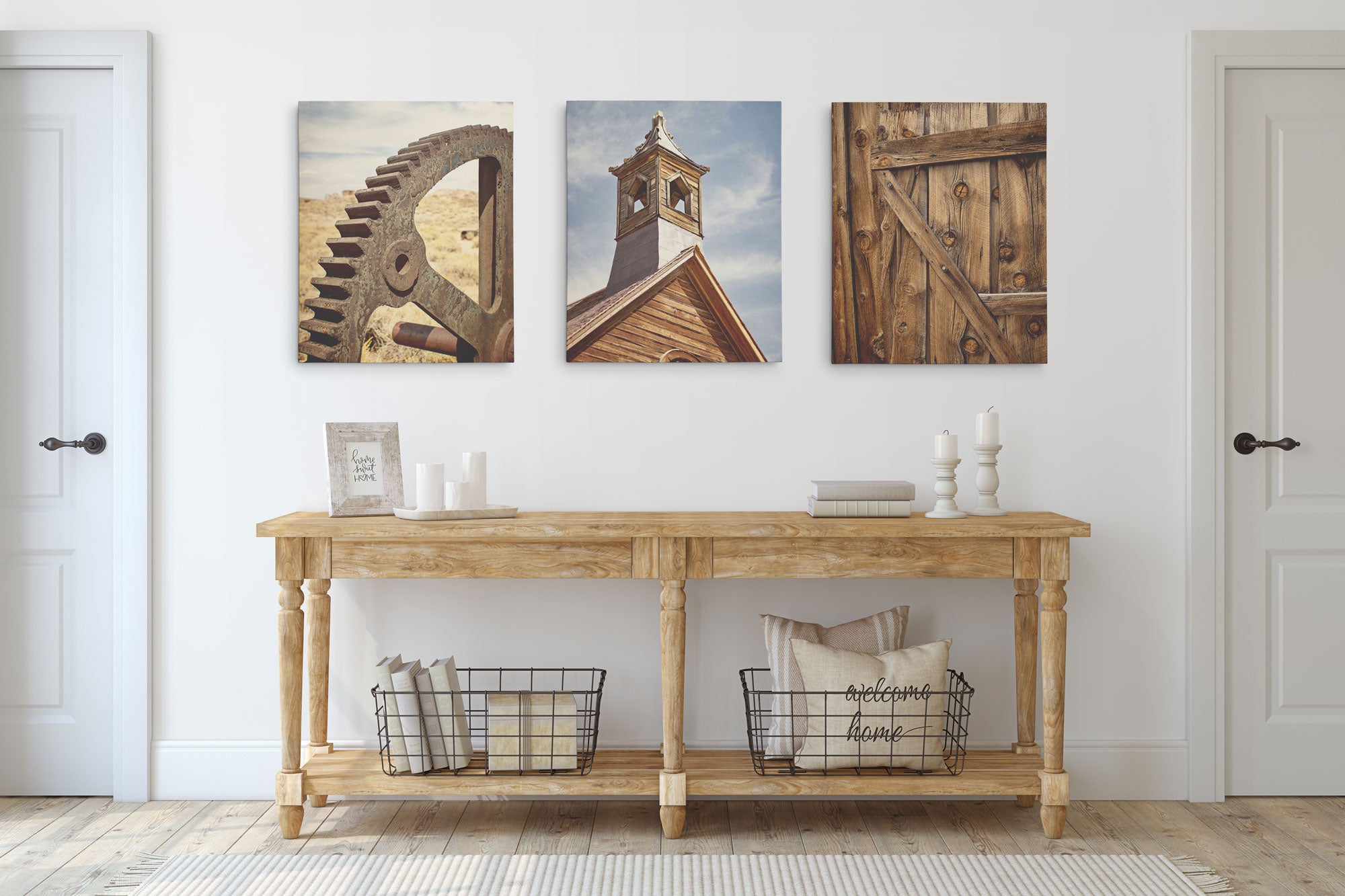 A wooden console table against a white wall displays Offley Green&#39;s Set of 3 Canvas featuring a gear, clock tower, and wooden door. The table also holds a framed quote, candles, white vases, and two wire baskets with pillows. Two closed doors flank the scene.