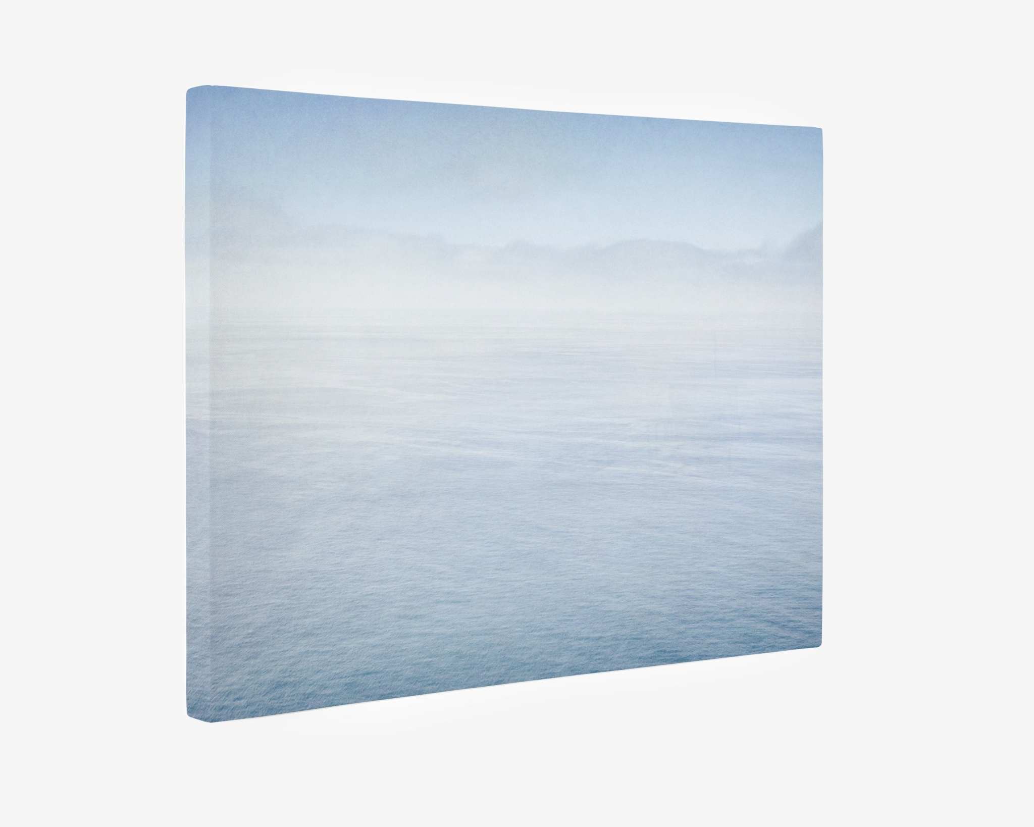 An Offley Green Abstract Blue Ocean Art, 'Soothing Blue Sea,' features a serene seascape with calm, light blue waters extending to the horizon. The misty sky merges seamlessly with the distant horizon, creating a sense of tranquility and endlessness reminiscent of the Big Sur ocean. The image is positioned against a plain white background.