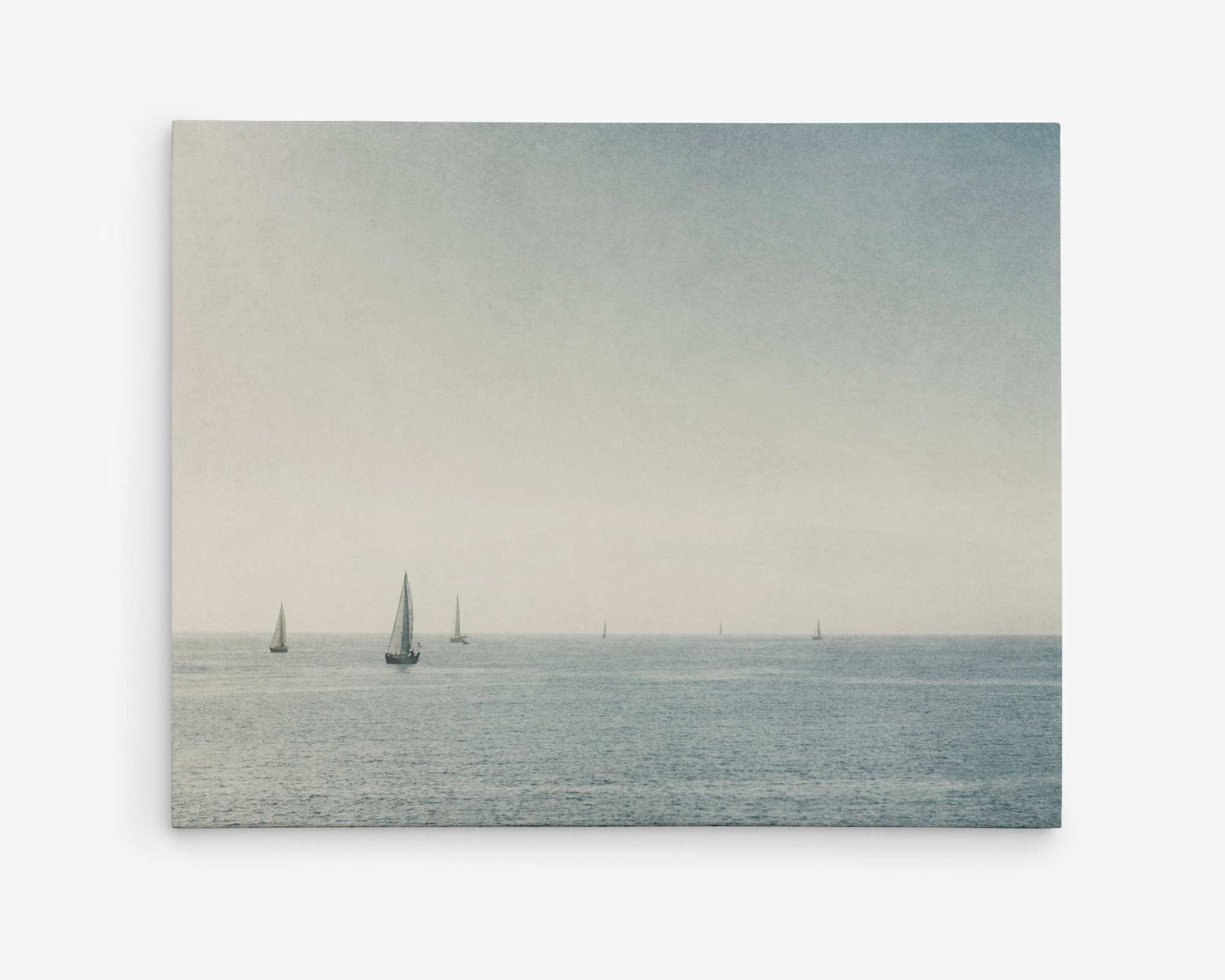 A serene ocean scene with several sailboats scattered across the calm water under a slightly overcast sky in Marina Del Rey. The horizon is faintly visible, blending seamlessly with the distant water surface. This Moody Nautical Seascape Canvas, 'Sail Boats Approaching' by Offley Green evokes a sense of tranquility and peacefulness.