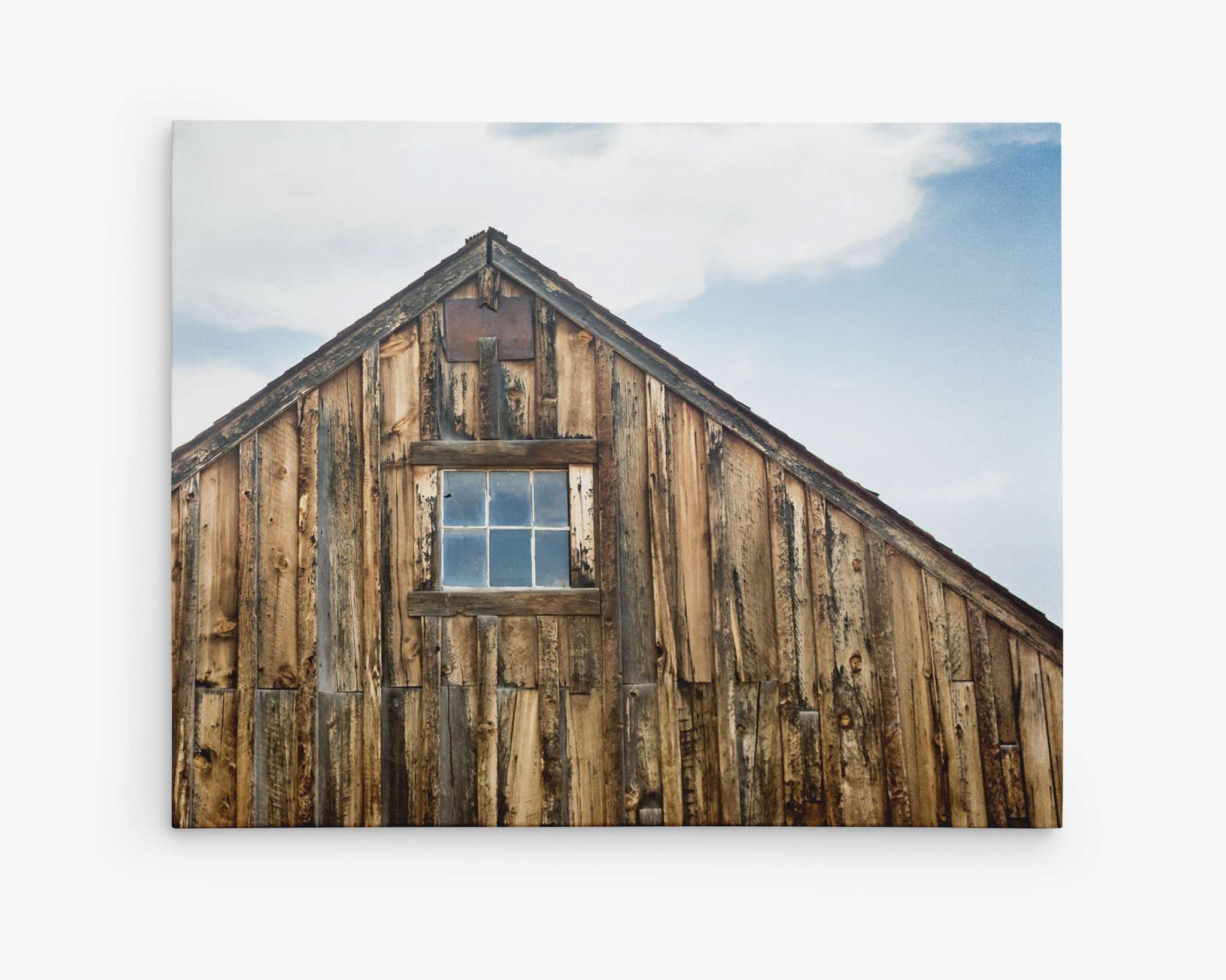 A close-up photograph of the upper portion of a rustic, weathered wooden barn with a single, small window in the center. The sky is partially cloudy in the background, captured beautifully on premium artist-grade canvas. This piece evokes the timeless charm of a rustic farmhouse. Introducing Farmhouse Wall Art, Rustic Barn Decor, 'Old Barn at Bodie' by Offley Green.