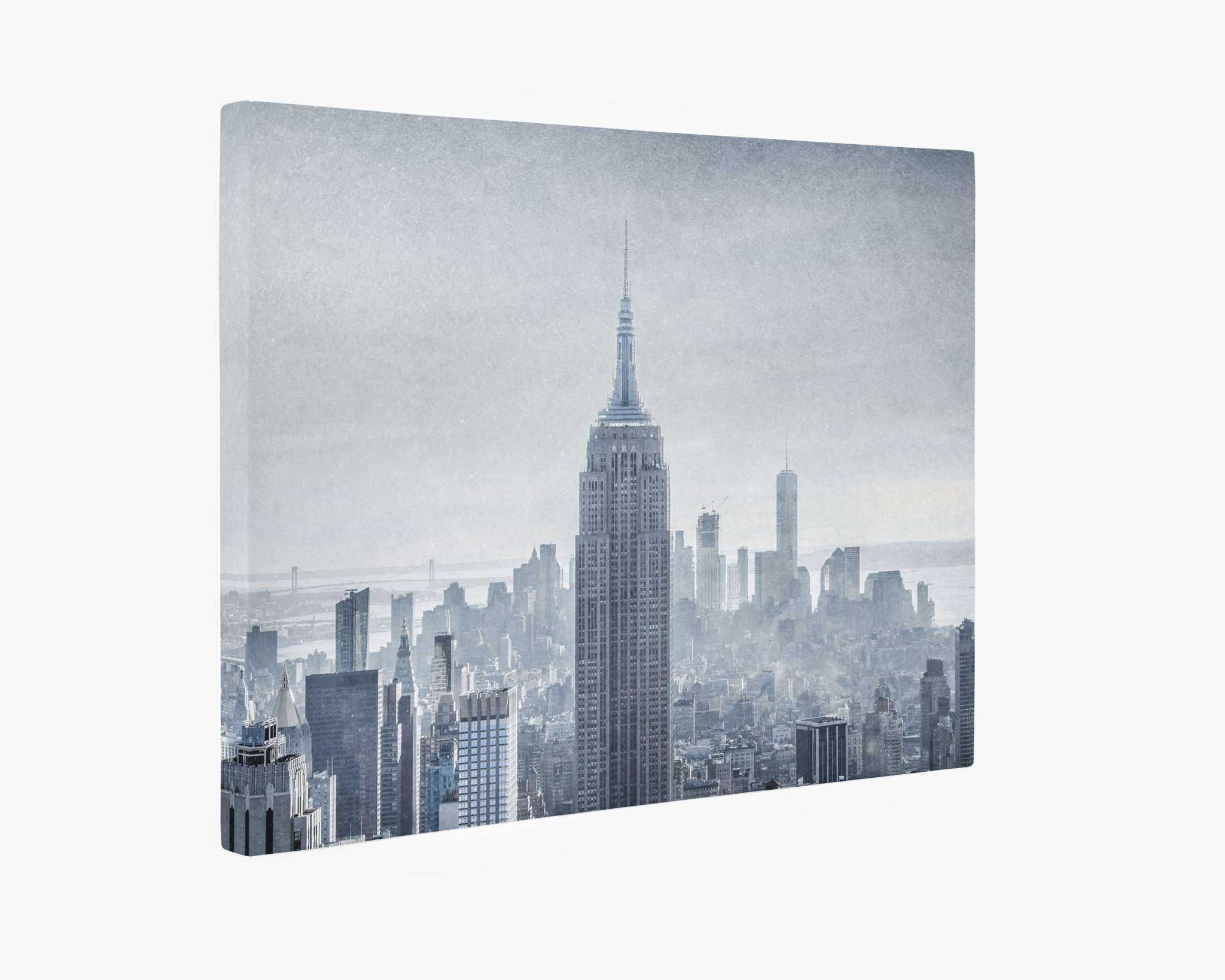 A large canvas gallery wrap showcases a grayscale image of New York City's skyline with the Empire State Building prominently centered. Misty weather lends a foggy atmosphere to the distant buildings, beautifully printed on a premium poly-cotton blend for added durability and vibrancy. The New York City Canvas Wall Art, 'Winter Metropolis' by Offley Green captures this mesmerizing scene perfectly.
