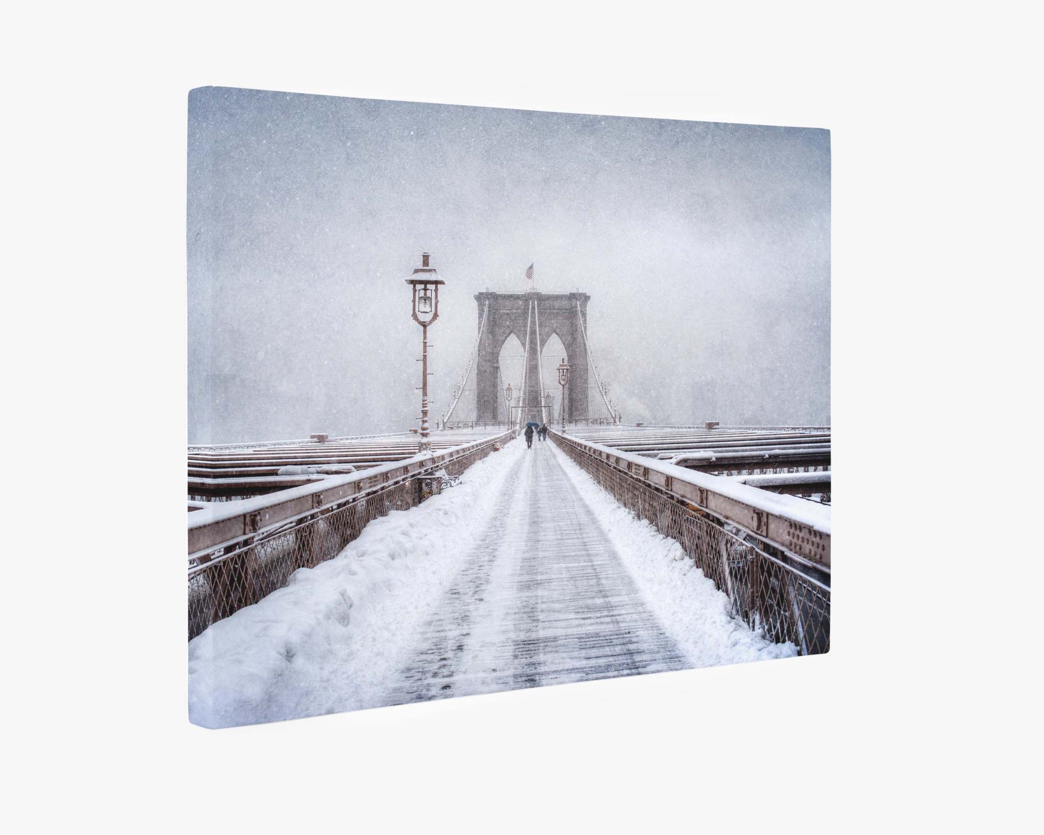 A wintery scene of the Brooklyn Bridge covered in snow, perfect for a Christmas card. The path is lined with a thin, undisturbed layer of snow, and lampposts are visible along the railing. The sky is overcast, and visibility is limited due to the falling snow. This picturesque view is beautifully captured in Offley Green's New York Brooklyn Wall Art, 'Brooklyn Snow'.