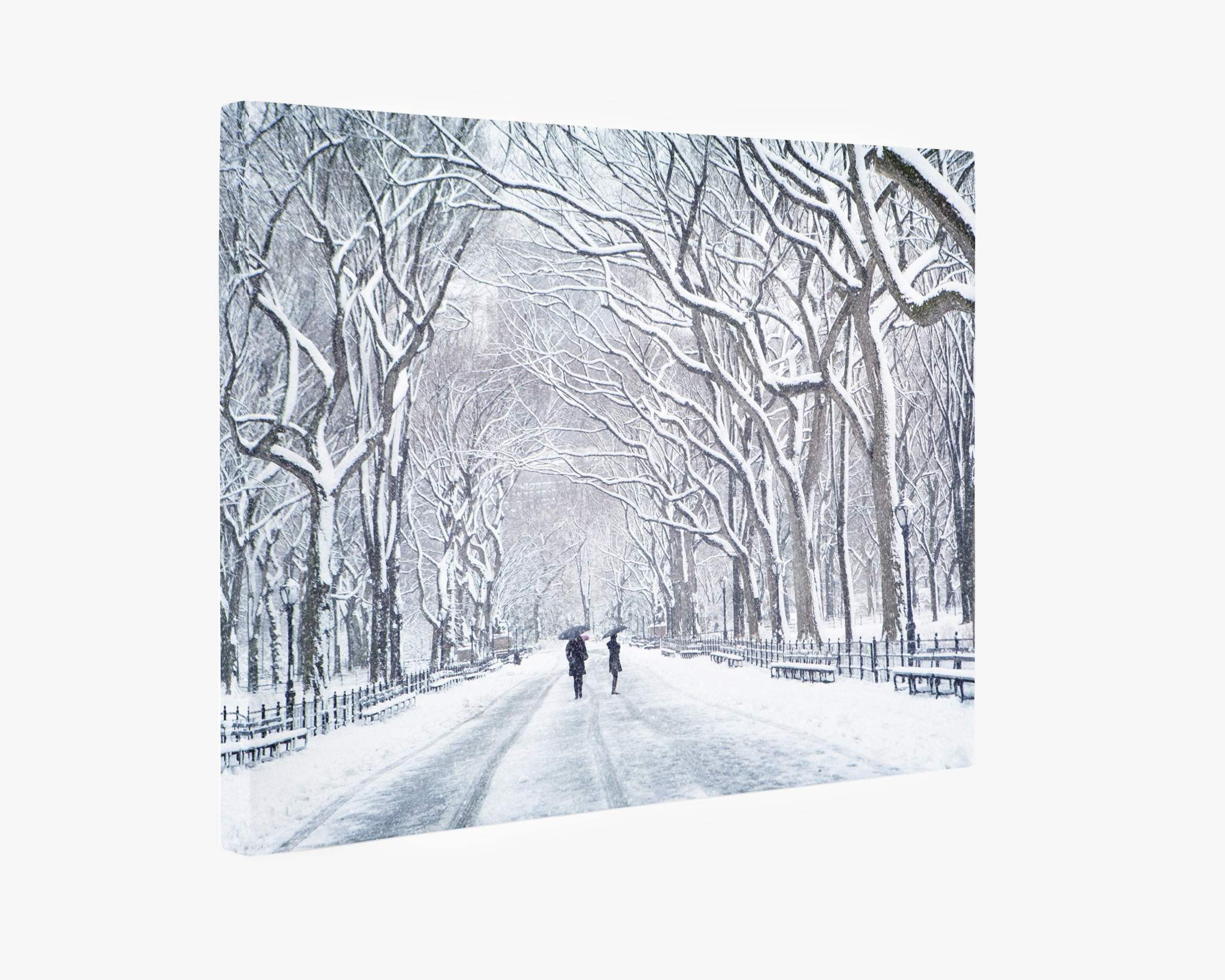 A winter scene depicting a snowy path flanked by leafless trees, captured on premium artist-grade canvas. Two individuals walk in the distance, bundled up against the cold. The branches are covered in fresh snow, creating a serene and quiet atmosphere. This Offley Green ready-to-hang solution, New York Central Park Wall Art, &#39;The Mall In Winter&#39;, adds elegance to any space.