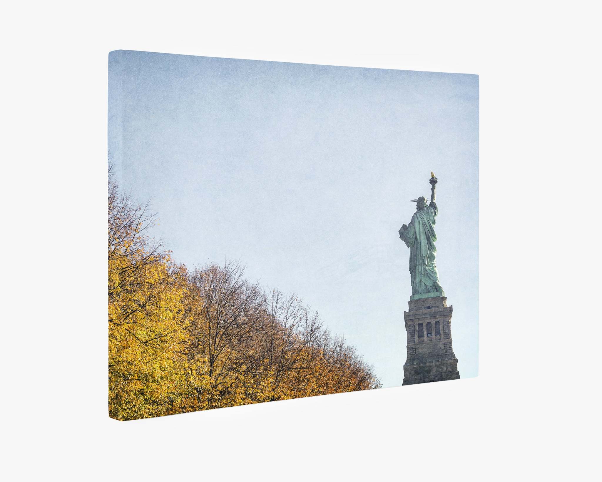 An Offley Green New York City Canvas Wall Art, &#39;Liberty in Fall&#39; is seen from a low angle, with its iconic torch raised in her right hand. To the left, leafless trees with yellow foliage are visible under a clear blue sky, all rendered on premium artist-grade canvas.