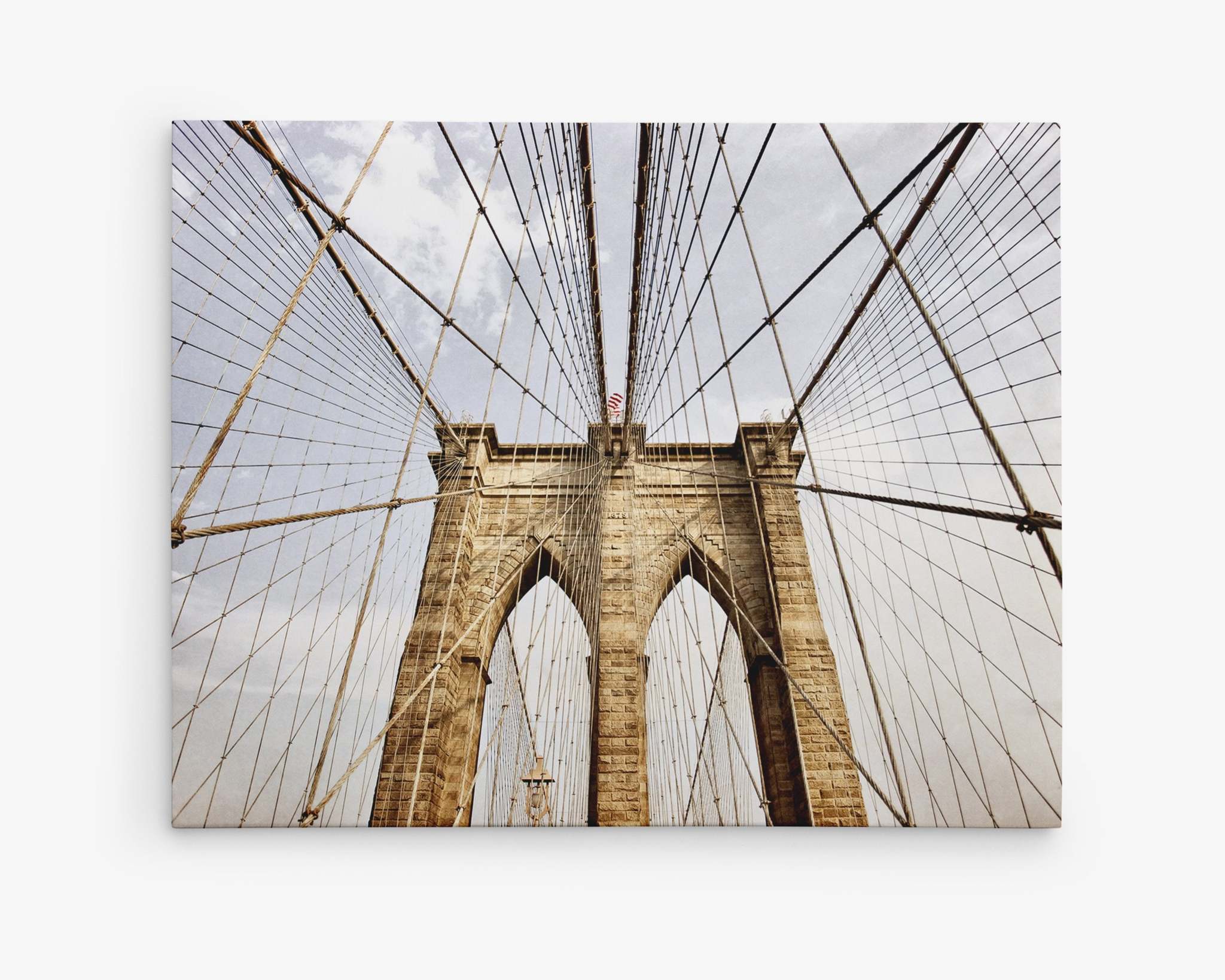 A low-angle view of the Brooklyn Bridge&#39;s stone arches and intricate cable system against a cloudy sky. The symmetrical design and perspective emphasize the bridge&#39;s architectural details and grandeur, all captured on premium artist-grade canvas for an exquisite finish with Offley Green&#39;s New York City Canvas Wall Art, &#39;Brooklyn Wires&#39;.